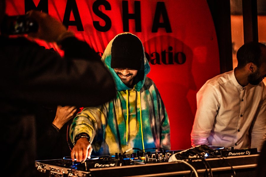 L.B.ONE performing in a colorful hoodie against a red backdrop