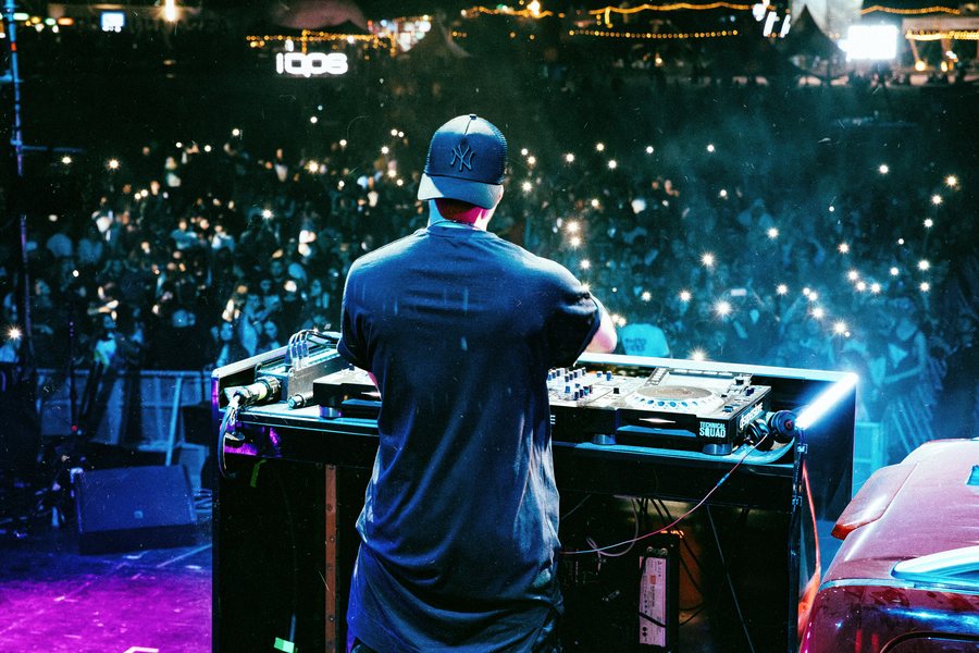 L.B.ONE behind the decks facing a crowd of phone lights