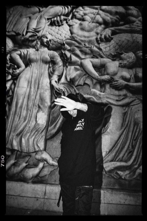 Black-and-white portrait of L.B.ONE in front of a sculpted wall